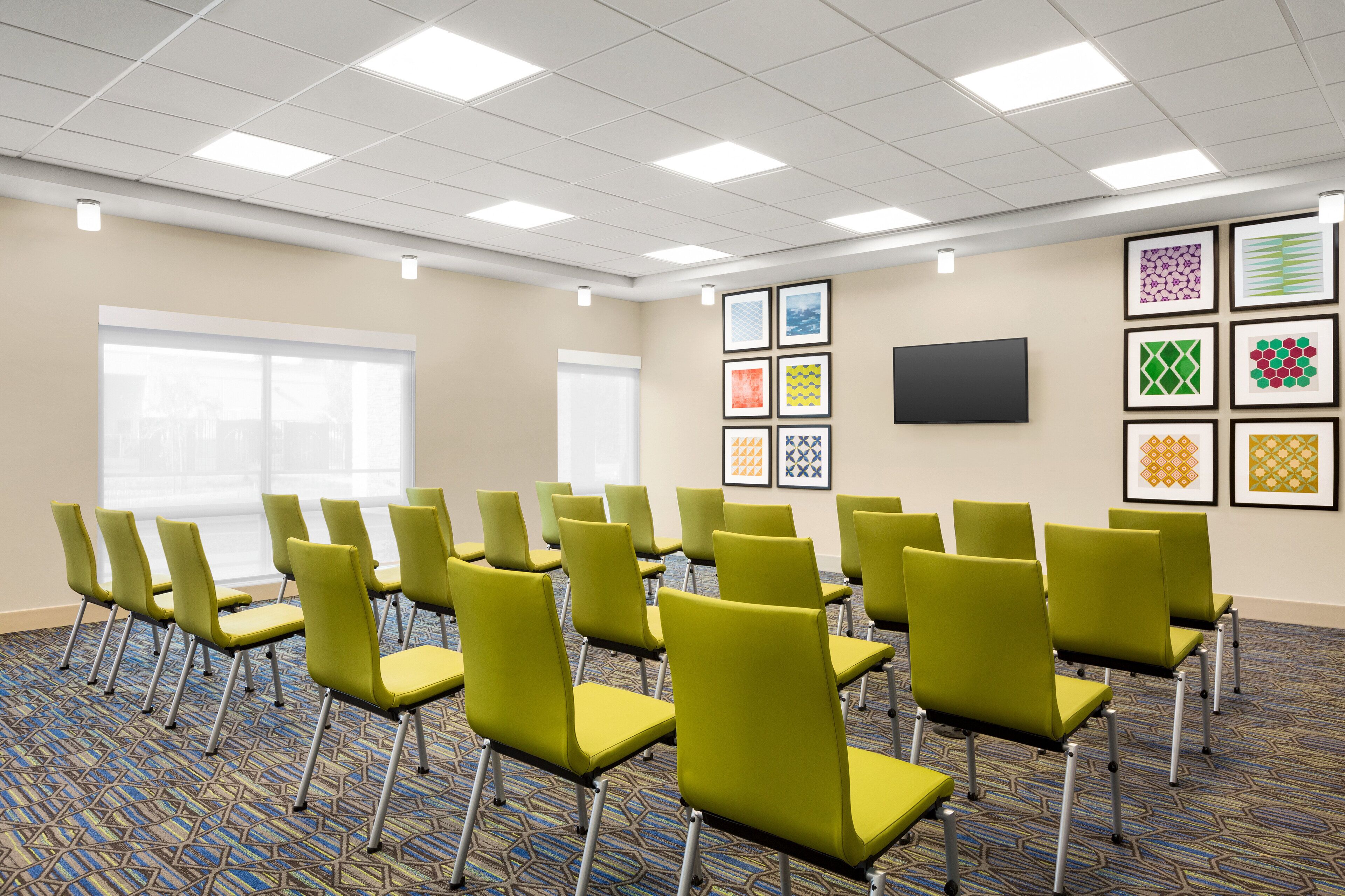 A conference room with green chairs, a large window, and framed artwork on the walls.
