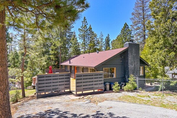 A cabin with a red roof, a stone chimney, and a wooden deck.