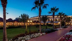 A hotel with multiple floors, a well-lit exterior, and a pathway lined with flowers and palm trees. - Club Hotel Turan Prince World Select Villa (Manavgat)