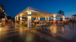 An outdoor dining area with tables and chairs, a covered seating area, and a view of the sea. - Club Hotel Turan Prince World Select Villa (Manavgat)