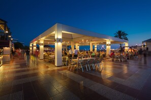 An outdoor dining area with tables and chairs, a covered seating area, and a view of the sea.