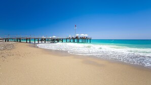 A beach with a pier extending into the ocean, featuring umbrellas and a flag. - Club Hotel Turan Prince World Select Villa (Manavgat)