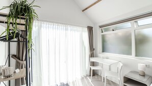 A modern room with a white table, chairs, a plant, and a window with frosted glass. - Be So Suite : Perfect getaway for 2 (Zandvoort)