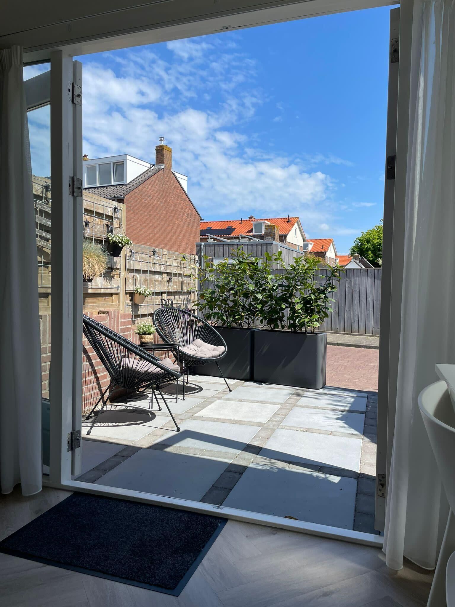 An open sliding door to a patio with two black wire-framed chairs, a potted plant, and a tiled floor.