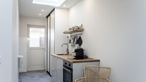 Une cuisine compacte dotée d’un puits de lumière, d’un four encastré, d’un petit coin repas avec une chaise en osier et d’une étagère contenant des ustensiles de cuisine.