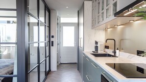 Cocina moderna con estufa integrada, un lavabo y armarios. Cuenta con una puerta corrediza de vidrio que da a un balcón con cama.