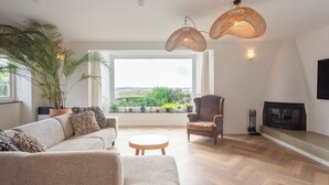 A living room with a sofa, armchair, round table, and a large window with a view of greenery. - Family villa behind the Beach. For 3 couples over 30 years old. (Zandvoort)