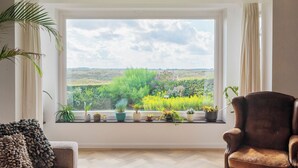 A room with a large window, a brown leather chair, a sofa, and various potted plants on the windowsill. - Family villa behind the Beach. For 3 couples over 30 years old. (Zandvoort)