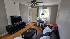 A living room with a TV, sofa, coffee table, and a dining area with a table and chairs. - Hel Stuga för 4 i Härlig Bymiljö (Dalarnas län)