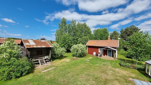 A rustic wooden cabin with a red roof, surrounded by lush greenery and trees. - Hel Stuga för 4 i Härlig Bymiljö (Dalarnas län)