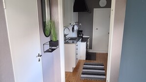 A hallway leading to a kitchen with a dark floor, a white door, a mirror, and a clock on the wall. - Hel Stuga för 4 i Härlig Bymiljö (Dalarnas län)
