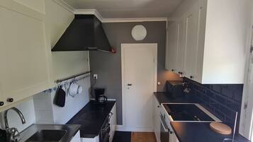 Una cocina compacta con armarios blancos, una estufa negra y una cafetera.