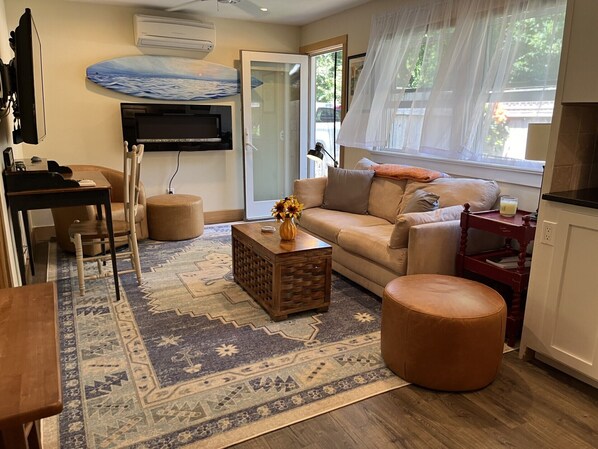 A living room with a sofa, ottoman, coffee table, and a TV mounted on the wall.