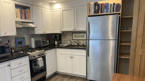 A modern kitchen with white cabinets, a stainless steel refrigerator, a gas stove, and a wooden dining table. - Charming Montauk Getaway centrally located  (Montauk)