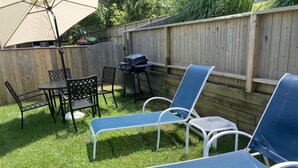 A backyard with a wooden fence, a grill, and outdoor furniture including two blue lounge chairs and a table with chairs. - Charming Montauk Getaway centrally located  (Montauk)