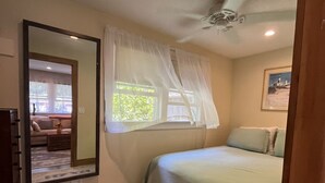 A bedroom with a bed, a large mirror, a window with sheer curtains, a ceiling fan, and a rug. - Charming Montauk Getaway centrally located  (Montauk)