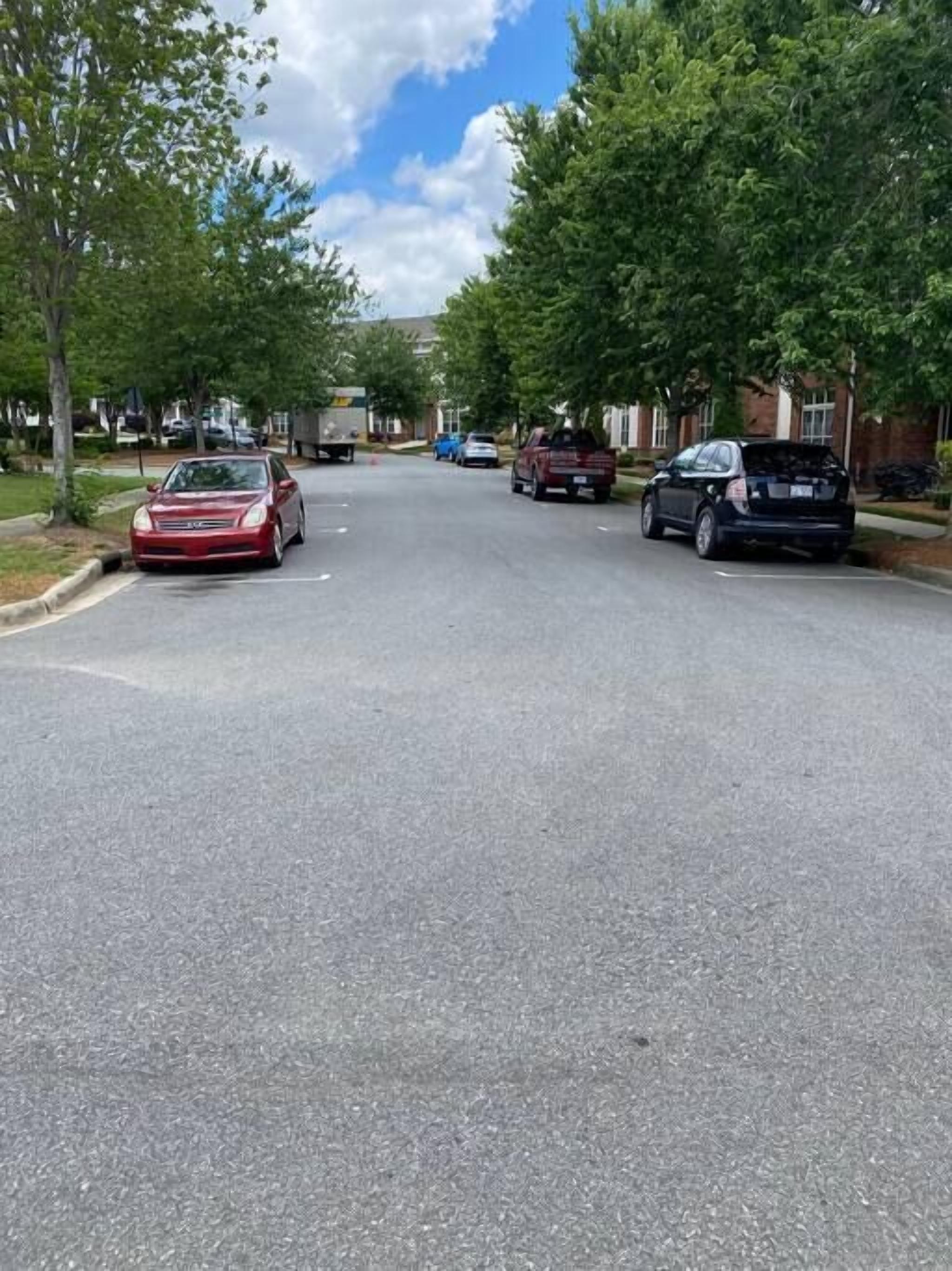 A residential street with parked cars and houses on both sides.