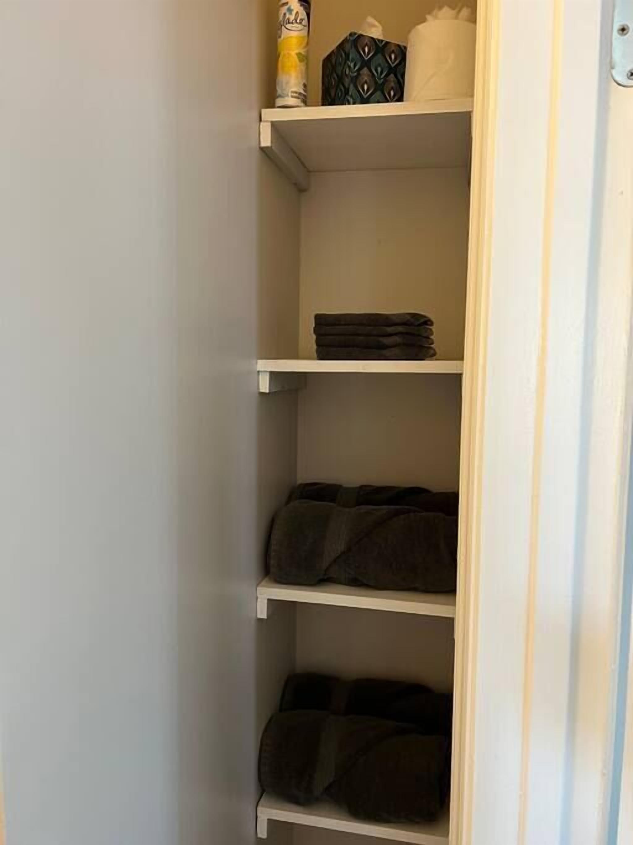 A closet with multiple shelves, some with folded clothes and a tissue box on the top shelf.