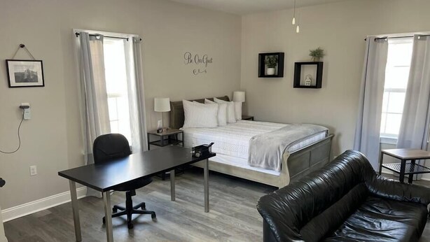 A modern hotel room with a bed, a desk, a leather sofa, and a marble coffee table.