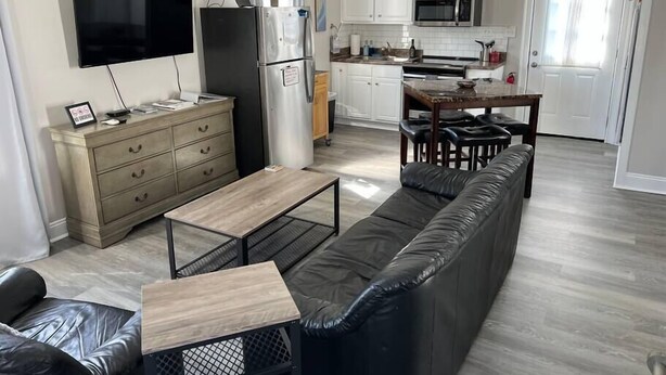 Uma sala moderna com sofá, mesa de centro, televisão, frigorífico e cozinha equipada com armários e micro-ondas.