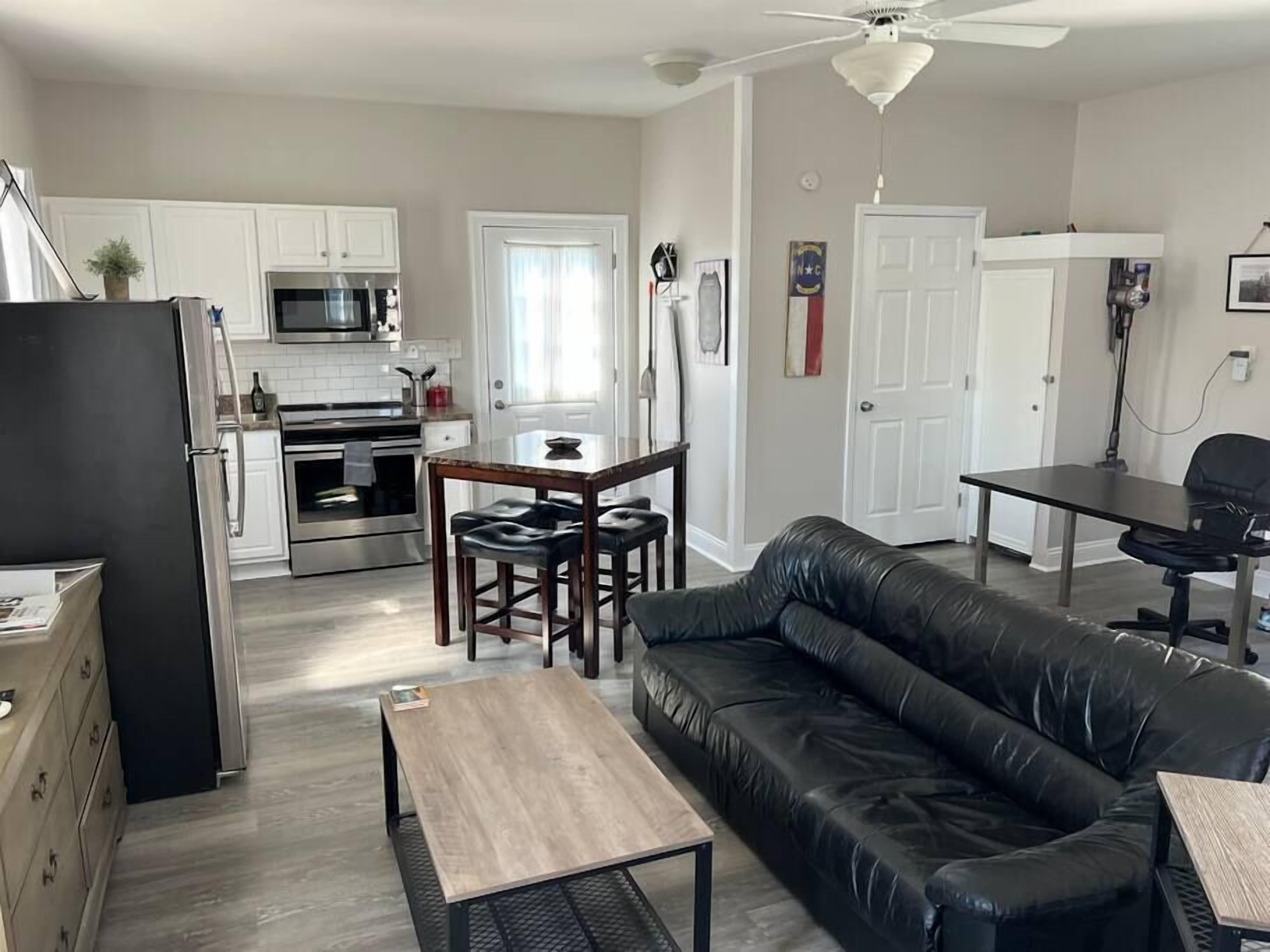 A modern kitchen with white cabinets, stainless steel appliances, and a dining area with a black leather couch and a wooden table.