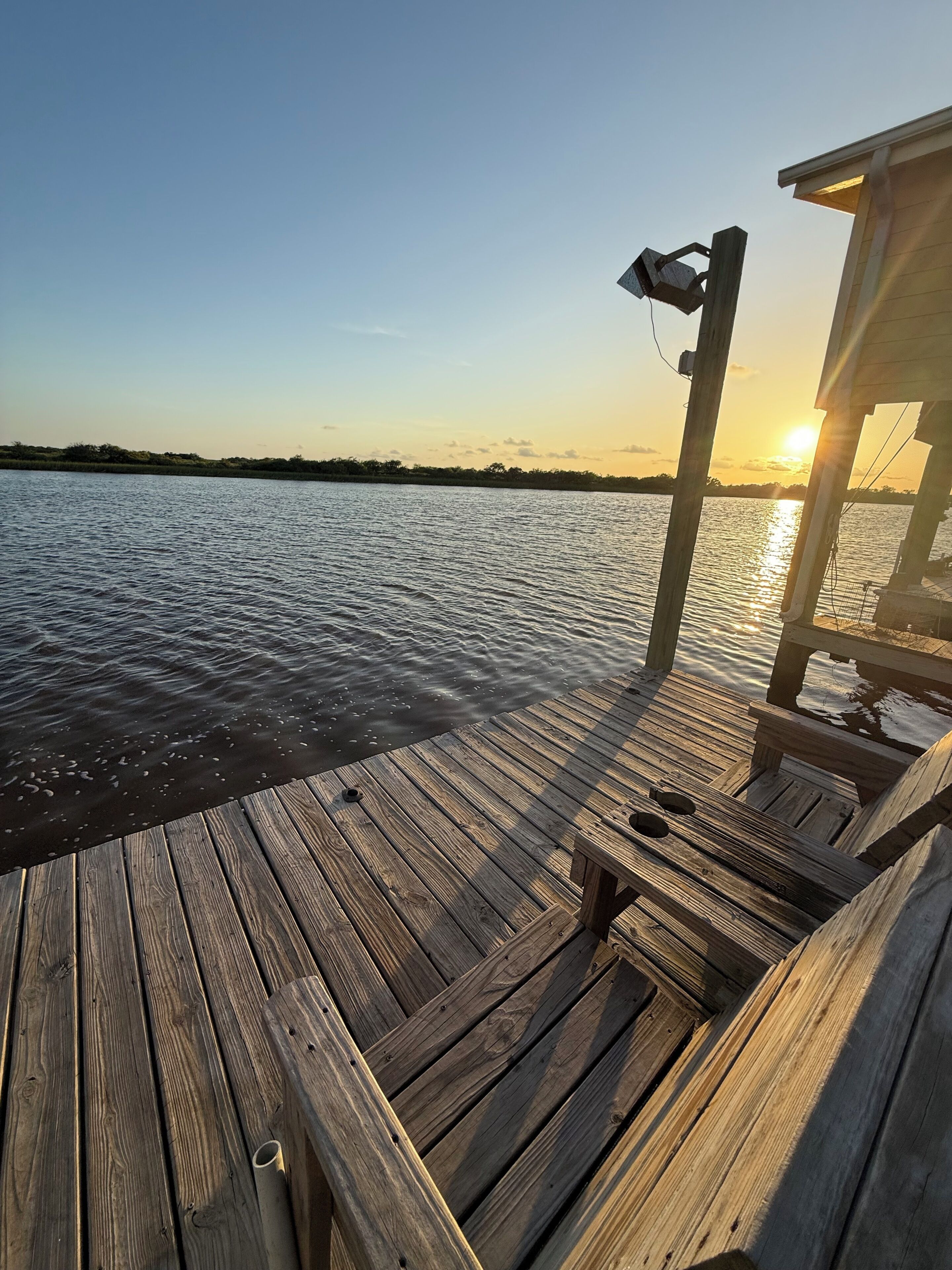 A wooden dock extending over calm water with a clear sky and a sunset in the background.