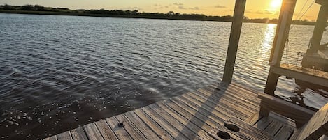 Une jetée en bois s’étendant au-dessus d’une étendue d’eau calme, avec un ciel dégagé et un coucher de soleil en arrière-plan.