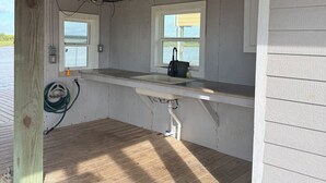A wooden deck with a white sink and window, under a wooden ceiling structure.