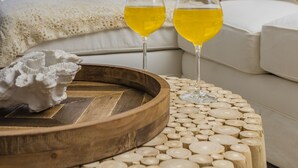 Een kamer met een bed, twee glazen gele drank en een houten dienblad op een ronde houten tafel.