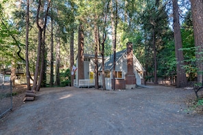 A cabin with a porch, surrounded by tall trees.