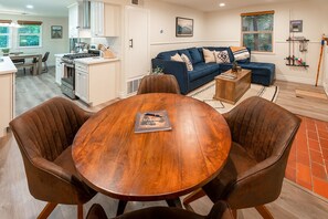 A modern living room with a blue sofa, a wooden dining table with four chairs, and a kitchen in the background.