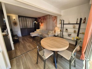 A modern living room with a round wooden table, two chairs, a sofa, and a decorative wall with a floral pattern.