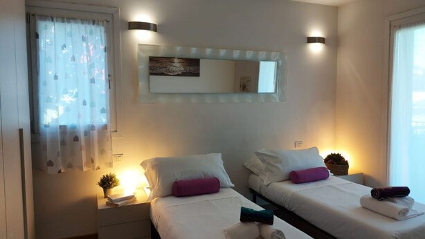 Une chambre d’hôtel avec deux lits, un grand miroir, des lampes de chevet, une petite plante et une fenêtre avec des rideaux.