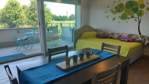 Une pièce comprenant un lit, une table à manger avec des chaises, un balcon avec du mobilier d’extérieur et un mur orné d’une fresque représentant un arbre.