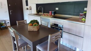 Une cuisine moderne avec des meubles blancs, un plan de travail foncé et une table à manger en bois, assortie de chaises.