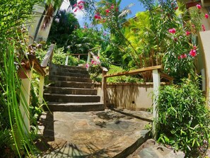 Un escalier en pierre menant à un bâtiment, entouré d’une végétation luxuriante et de plantes en fleurs.