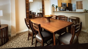 Ein Essbereich mit Holztisch und -stühlen, einer zentralen Schüssel und einer Küche im Hintergrund.