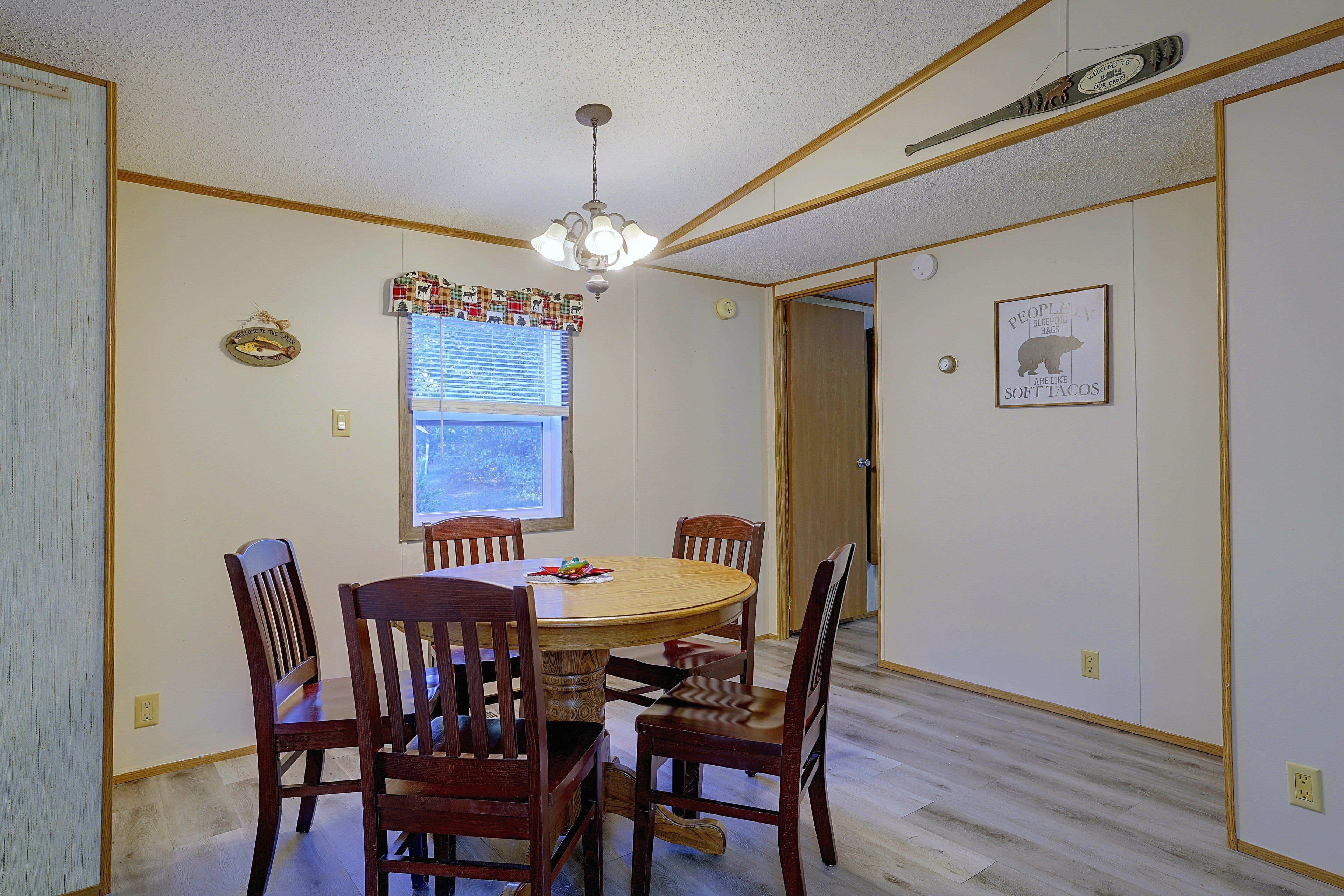 A dining room with a round table, wooden chairs, a chandelier, and a window with blinds.