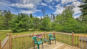 A wooden deck with two green chairs and a small table, surrounded by a wooden railing, overlooking a grassy area with trees and a clear sky. - Secluded Woodsy Cabin: Hike, Fish, Hunt + ATV! (Arkdale)