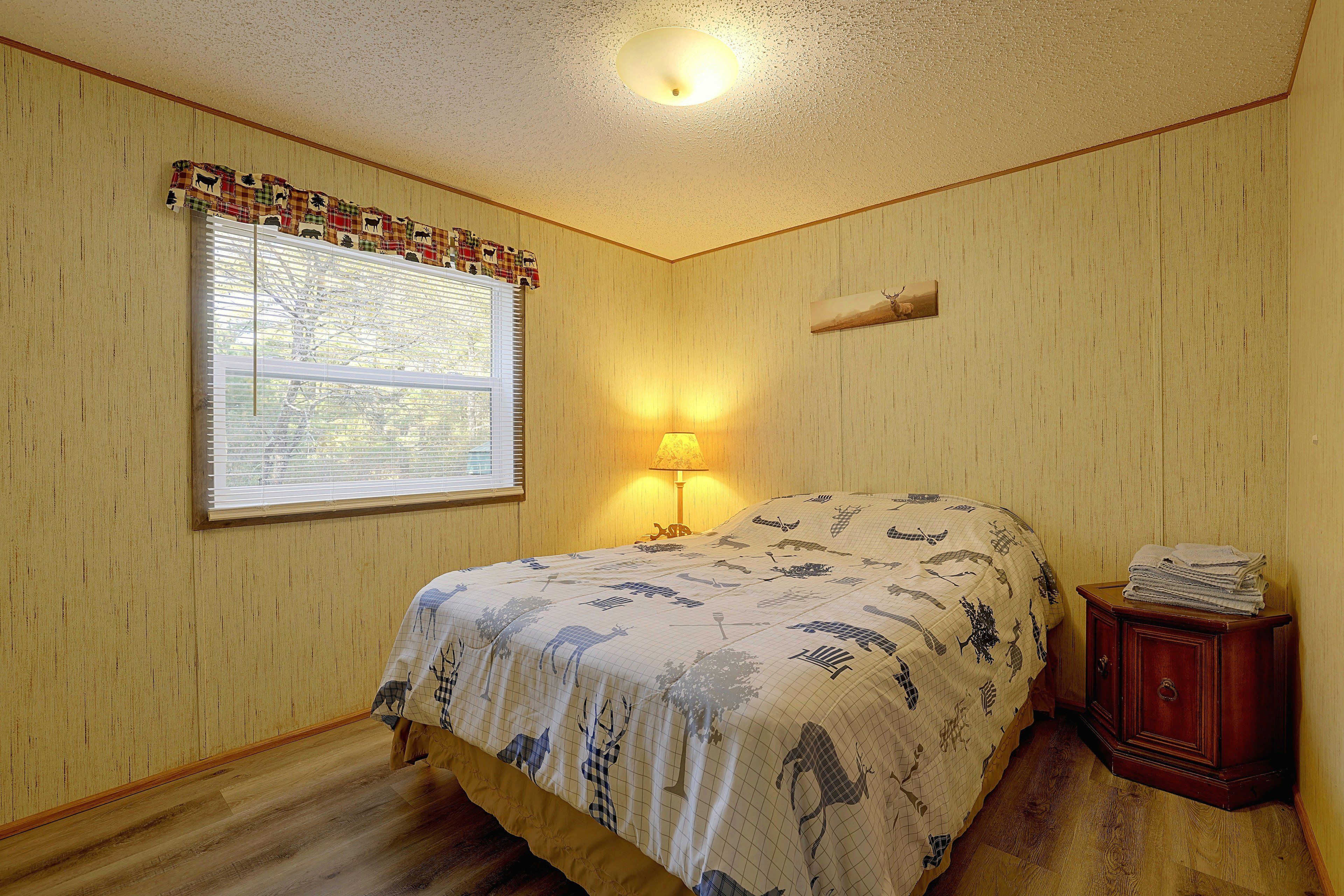 Une chambre à coucher avec un lit, une fenêtre avec des stores, une lampe de chevet et une table de chevet en bois.