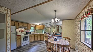 A spacious kitchen with wooden cabinets, a dining table with chairs, and a large window with curtains. - Secluded Woodsy Cabin: Hike, Fish, Hunt + ATV! (Arkdale)