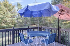 Une terrasse en bois avec une table et des chaises, un parasol bleu et un parasol rouge.