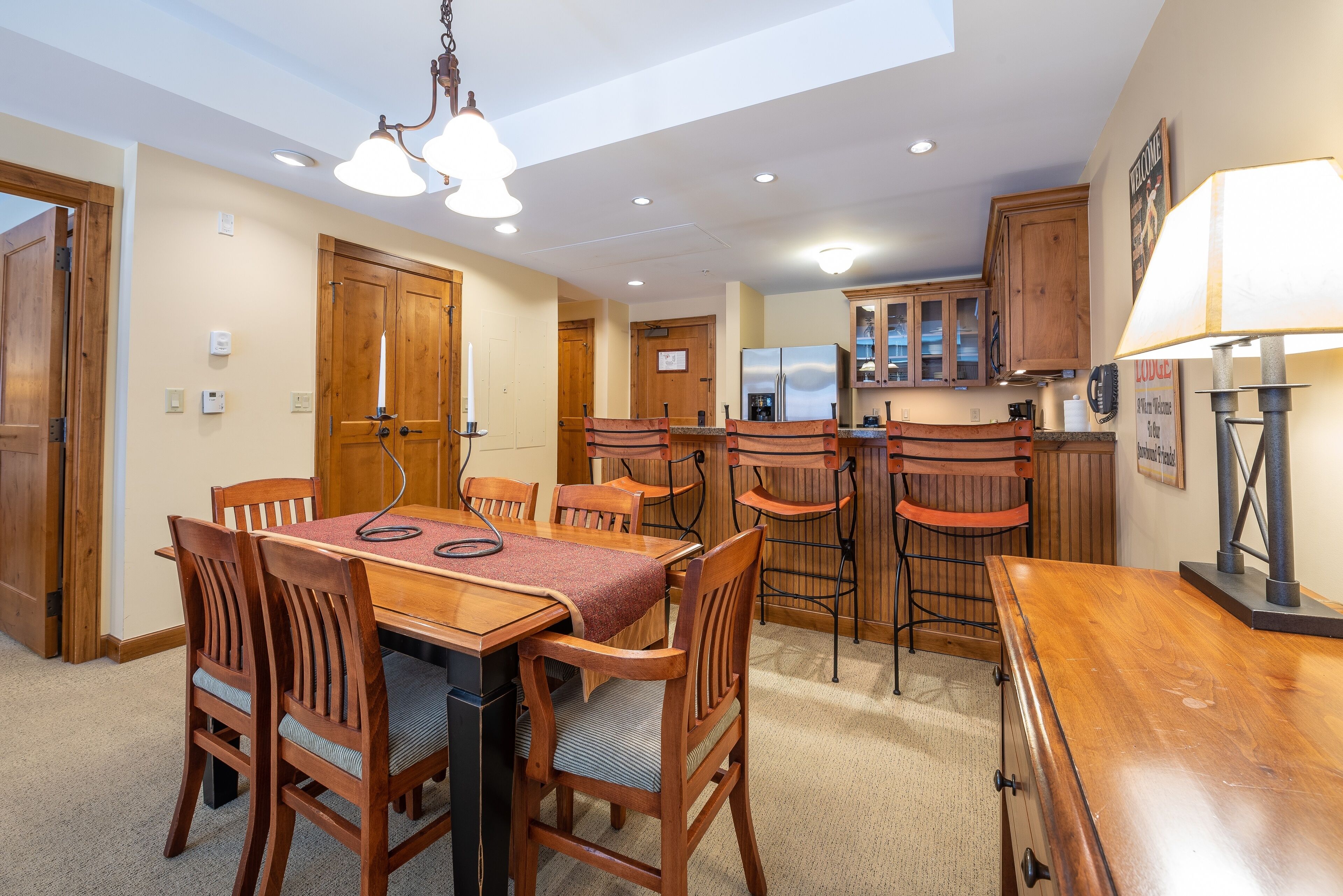 Un comedor con una mesa y sillas de madera, una cocina con armarios de madera y una lámpara de techo.