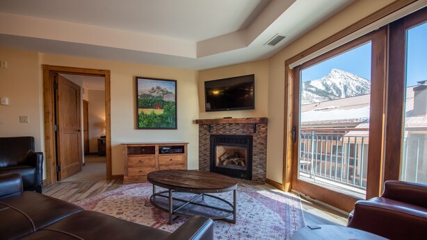 A living room with a fireplace, a television, and a view of mountains through large windows.