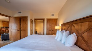 A large bed with white linens, wooden headboard, and multiple pillows. There are wooden doors and a lamp on the nightstand.