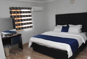 Een slaapkamer met een bed, een bureau en een raam met jaloezieën.