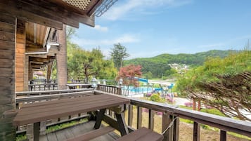 A wooden deck with picnic tables overlooking a pool area and a mountainous landscape.