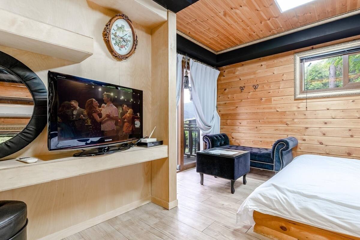 A cozy room with a bed, a TV, a wooden wall, and a window.