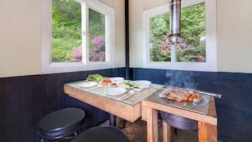 A small kitchen area with a grill, dining table, and two stools.