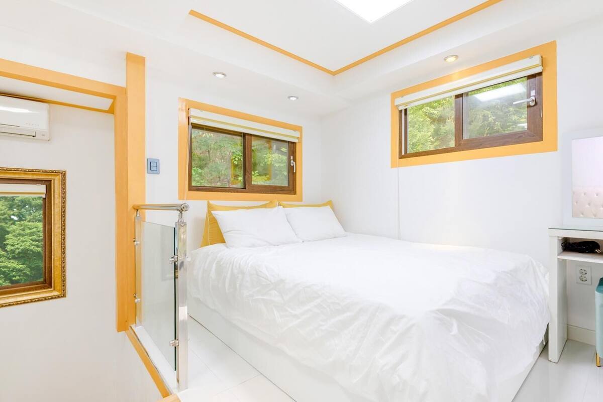 A bedroom with a bed, a desk, and a window with a view of greenery.